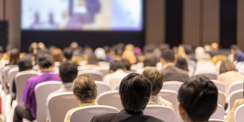 rear-view-of-audience-listening-speakers-on-the-stage-in-the-conference-hall-or-seminar-meeting-e1700247684380.jpg
